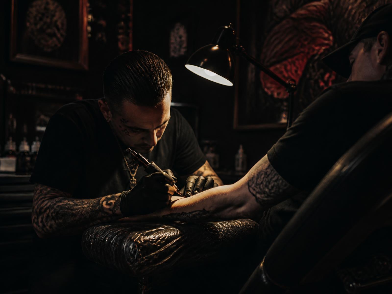 Tattoo artist at Déjà Vu Bedworth inking a client's forearm under a warm studio lamp